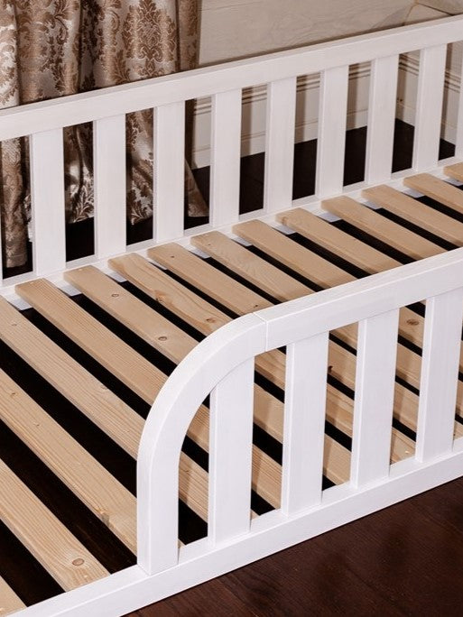 Toddler floor bed with rounded opening for kids safety - wooden bed frame with slats and rails. Close up white bed frame.