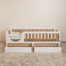 Front view of EZRA Montessori toddler bed with oak veneer rails and two open storage drawers