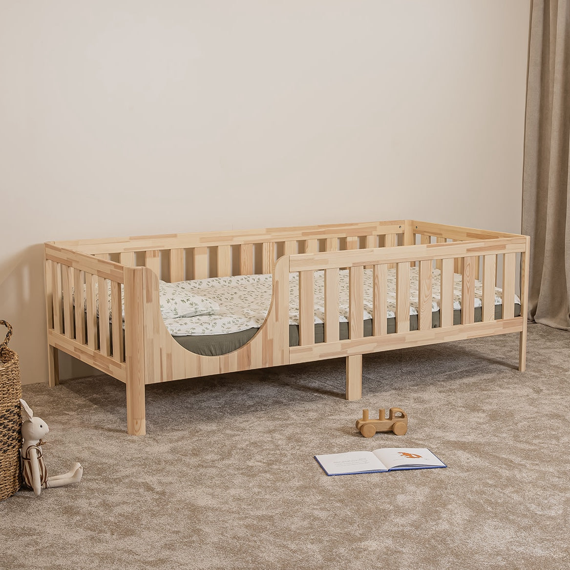 Angled view of EZRA Montessori toddler bed on legs with rounded entrance and natural pine safety rails