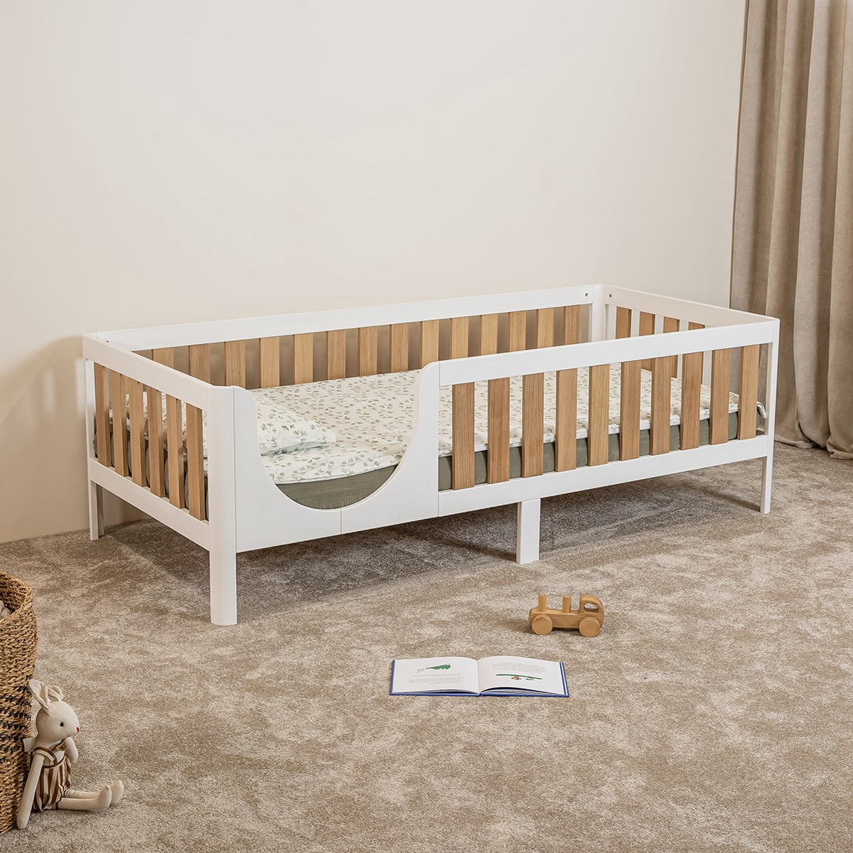 Angled view of EZRA Montessori toddler bed on legs with white frame and oak veneer rails