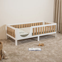 Angled view of EZRA Montessori toddler bed on legs with white frame and oak veneer rails