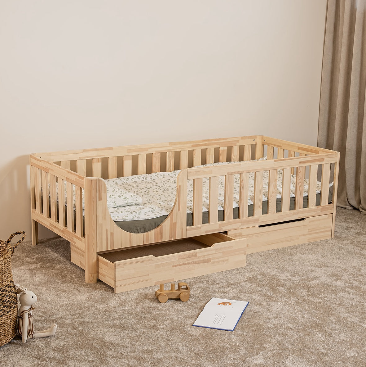 Angled view of EZRA Montessori toddler bed on legs with rounded entrance and one open under-bed storage drawer