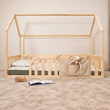 Beige Montessori bedside organiser with three pockets and a soft bunny, attached to a Montessori natural pine house floor bed in a child's bedroom.