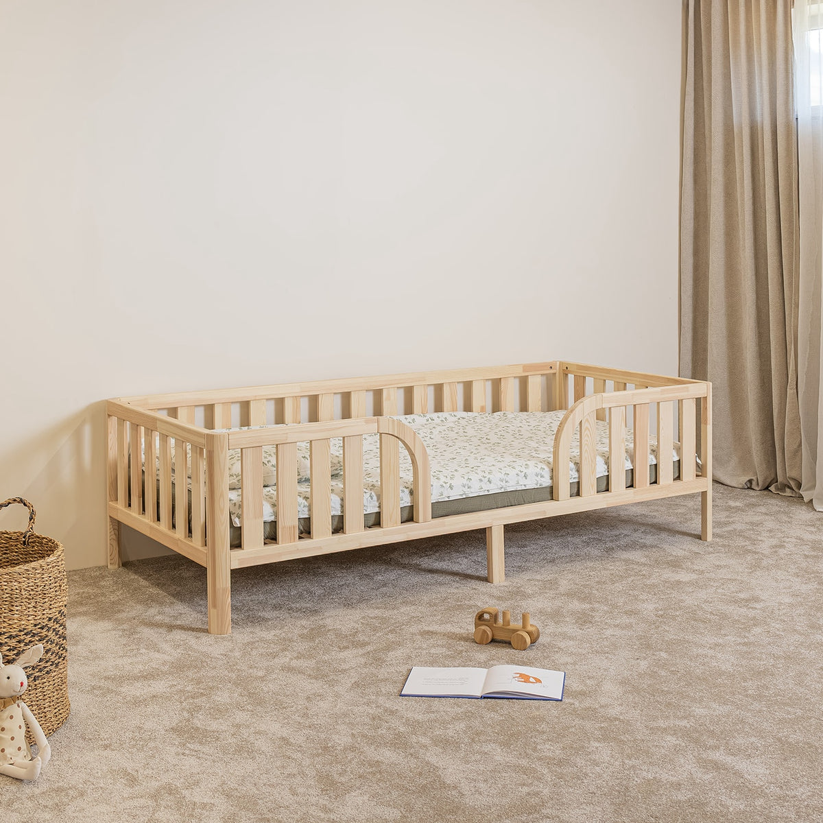 Angled view of Montessori toddler bed on legs with rounded middle opening and safety rails