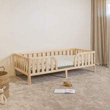 Angled view of Montessori toddler bed on legs with rounded middle opening and safety rails