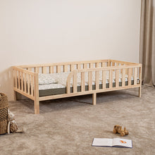 Montessori toddler bed on legs with rounded opening in natural wood, angled view