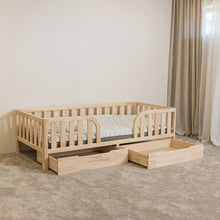 Angled view of Montessori toddler bed with rounded middle opening and two open storage drawers