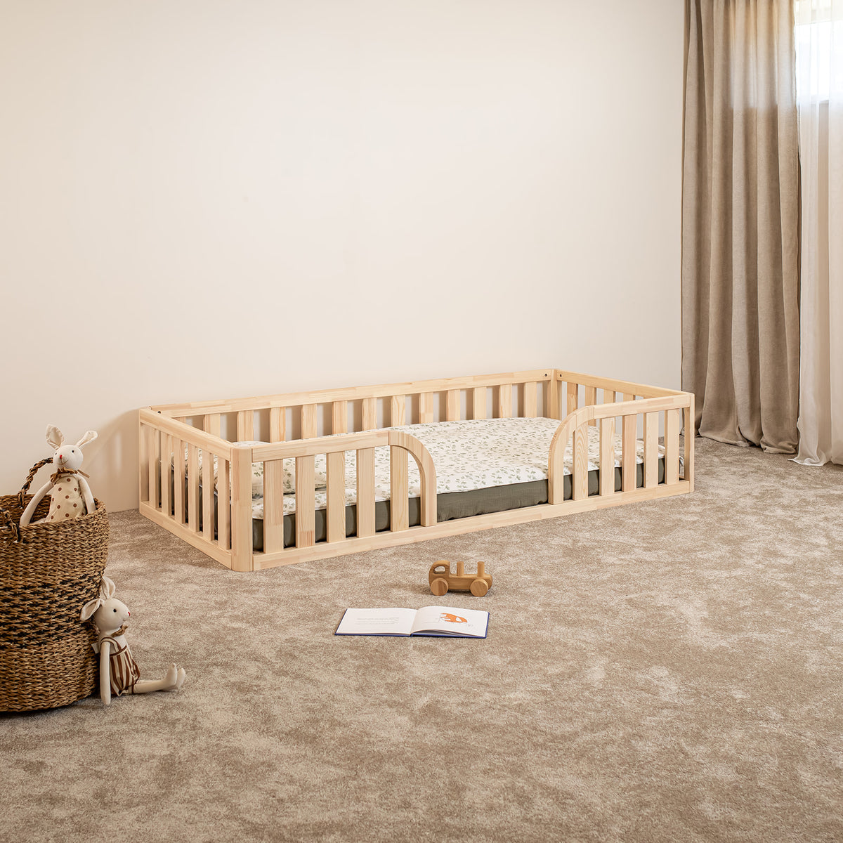 Angled view of Montessori toddler floor bed with rounded middle opening and safety rails in natural wood