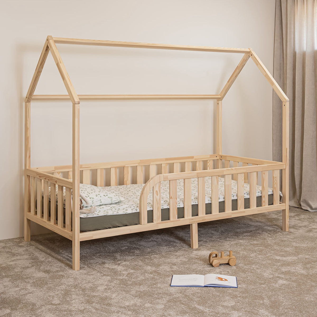 Angled view of Montessori toddler house bed on legs with rounded opening and natural pine safety rails