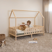 Child playing on Montessori toddler house bed on legs with rounded opening and natural wood safety rails