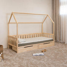 Angled view of Montessori toddler house bed on legs with open front side and two closed storage drawers