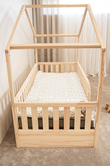 Side view of NOLRI Montessori toddler house bed with natural pine frame, safety rails and integrated storage