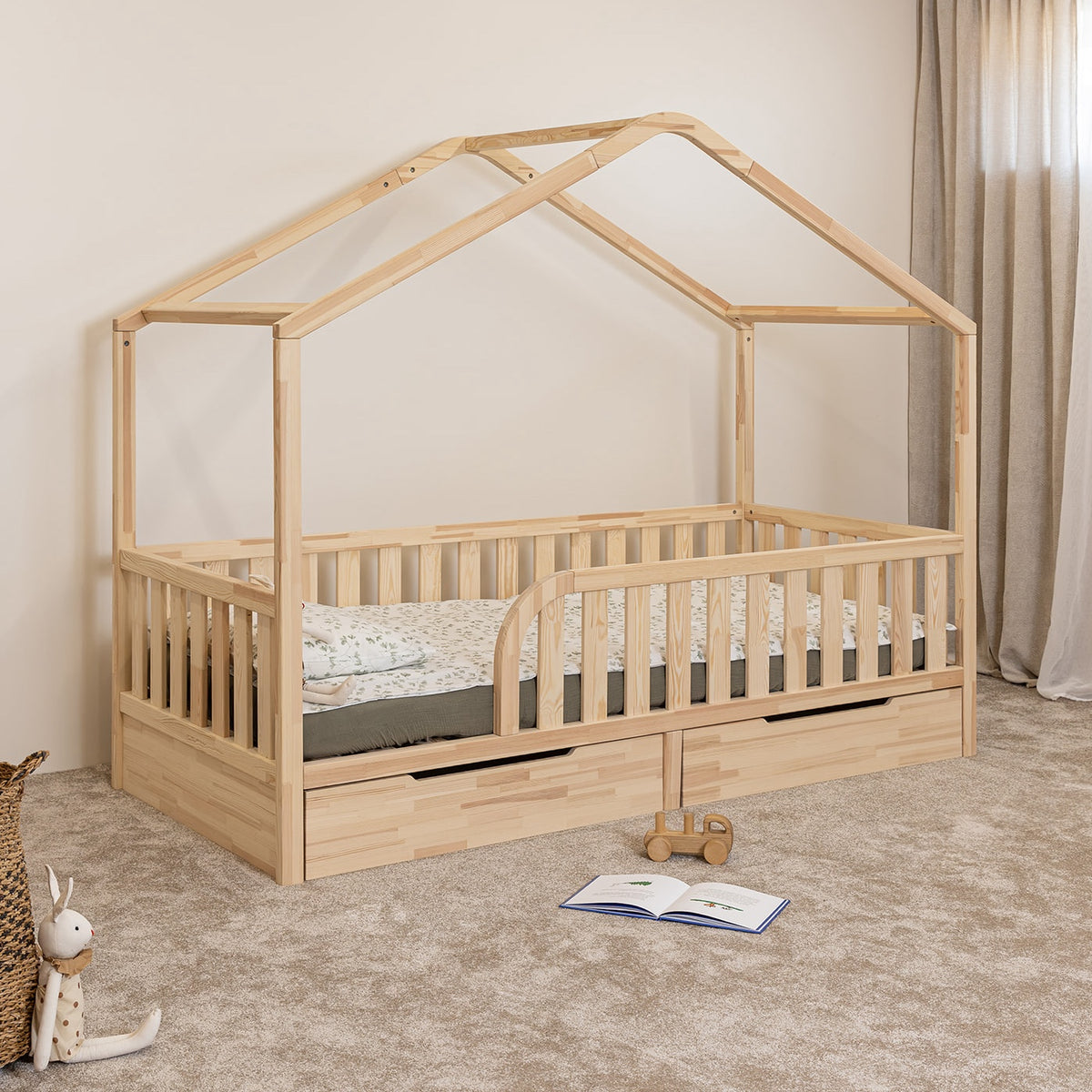 Angled view of NOLRI Montessori toddler house bed with rounded opening and two closed storage drawers