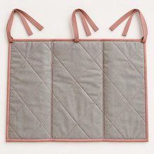 Back view of a quilted fabric bedside organiser with diamond stitching and three pairs of clay pink attachment ties.