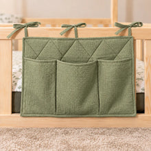 Close-up of a olive green quilted cotton bed pocket organiser with three storage pockets and fabric ties on a wooden bed railing.