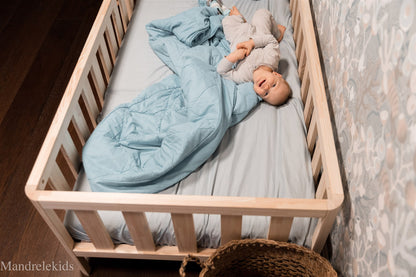 Top view of a wooden Montessori toddler bed with rails and a child lying on the mattress