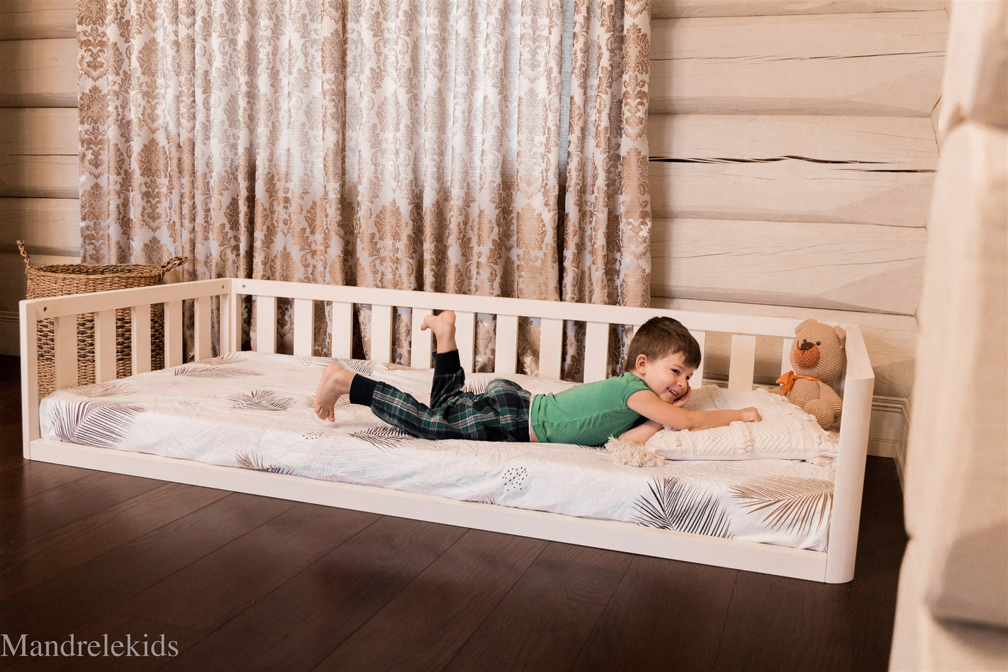 White Montessori toddler floor bed with rails and a child lying on the mattress