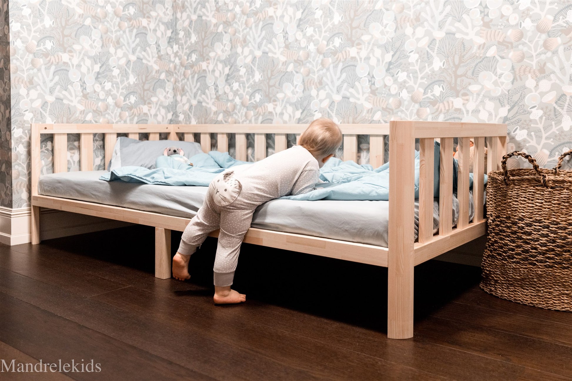 Wooden Montessori toddler bed on legs with rails and a child climbing into bed